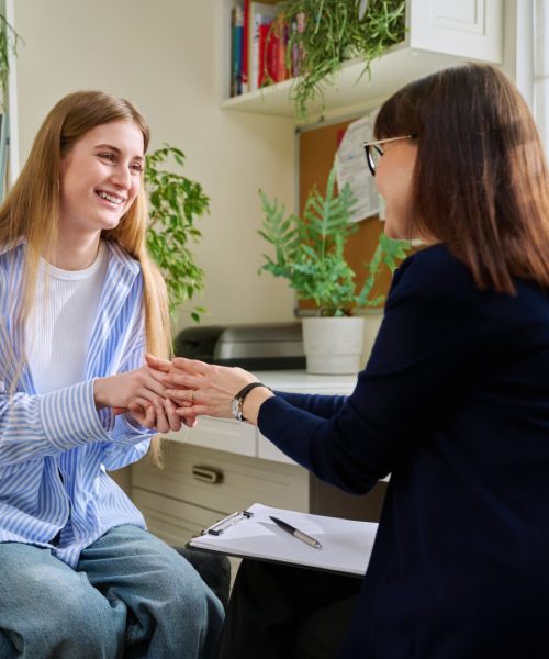 Smiling positive young teen female patient talking to professional mental therapist. Teenager girl high school college student in therapy with psychologist psychotherapist counselor. Treatment support