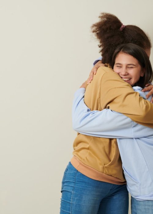 Happy teenage girls in jeans and hoodies hugging each other to express love